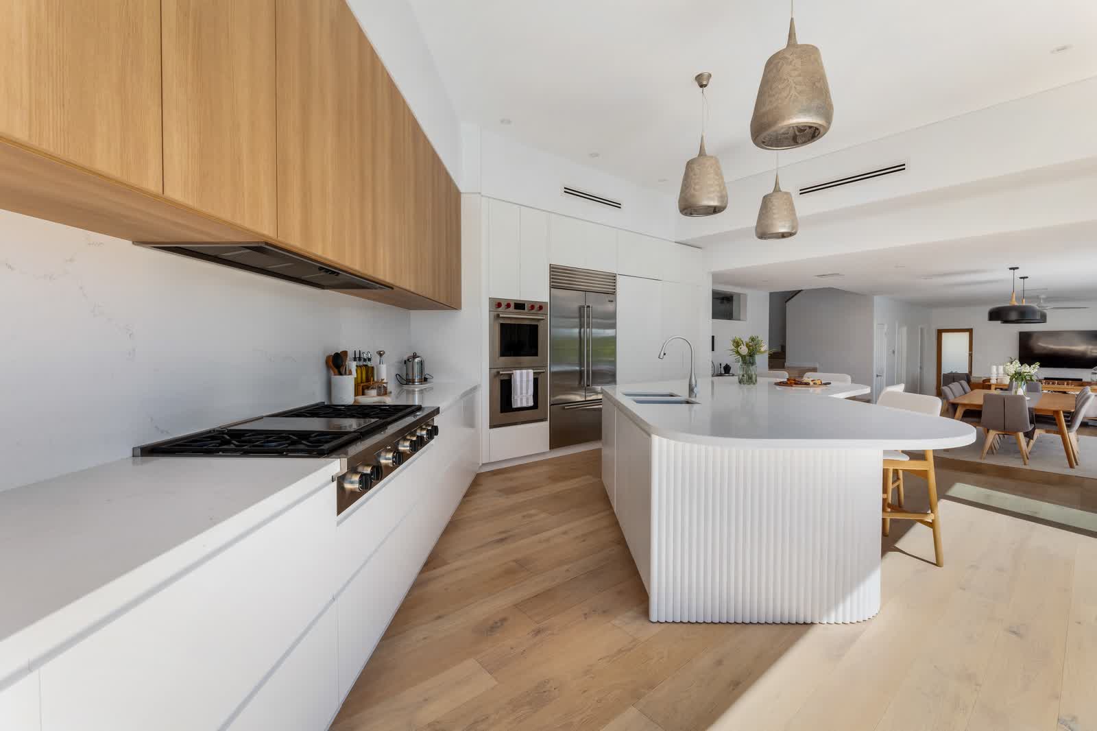 Renovated white kitchen with timber overheads and a curved island