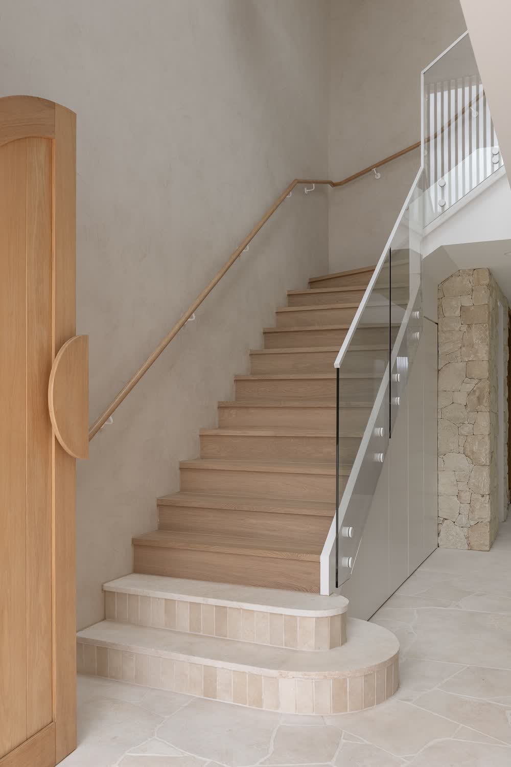 Timber stairs with a glass balustrade and sandstone wall